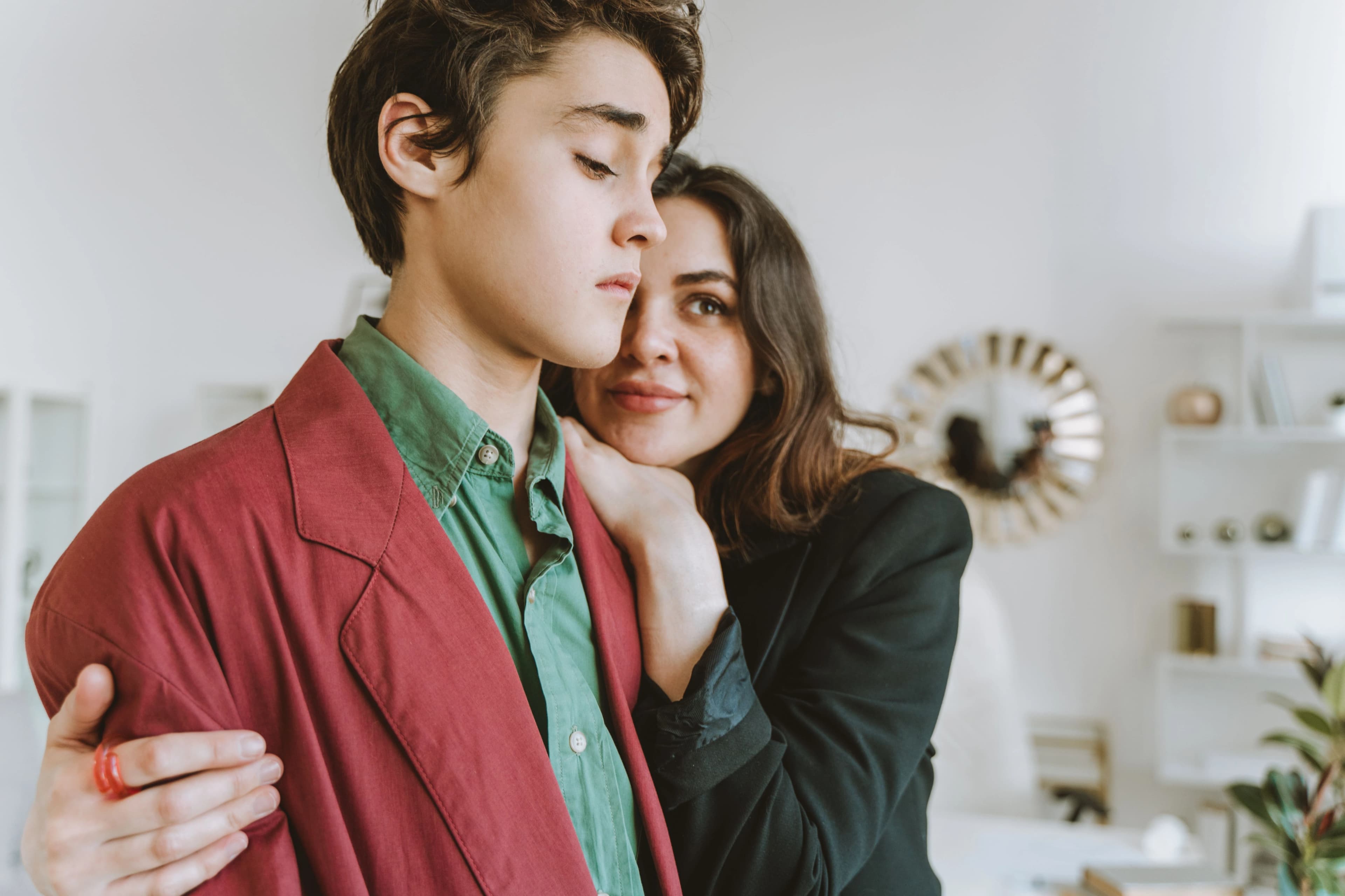 Une mère enlace tendrement son fils adolescent dans le salon, un moment de complicité.
