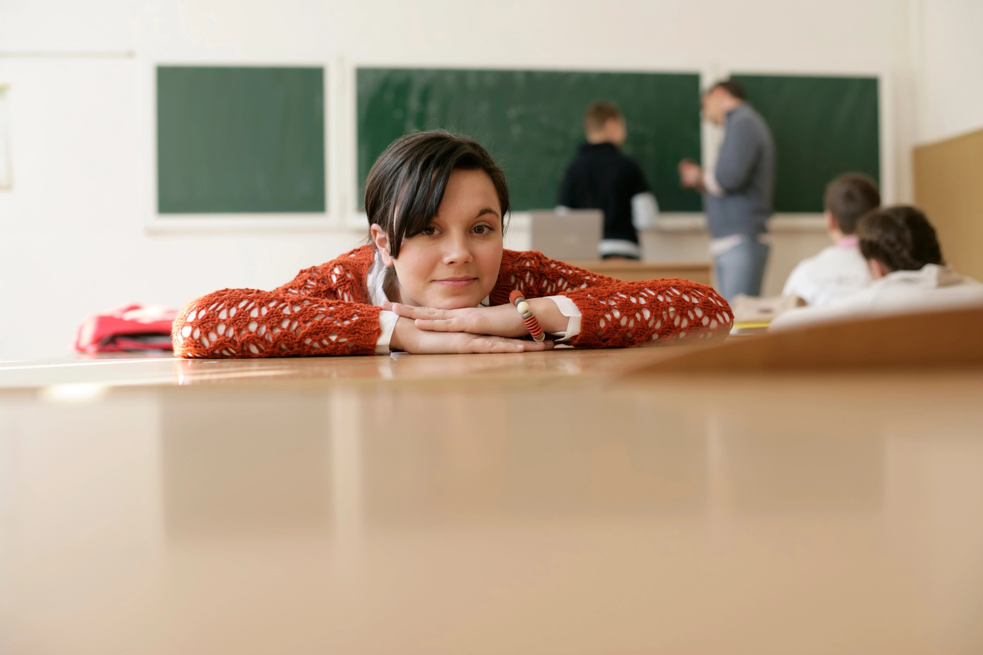 Une lycéenne pensive, la tête posée sur ses bras, à sa table pendant un cours.