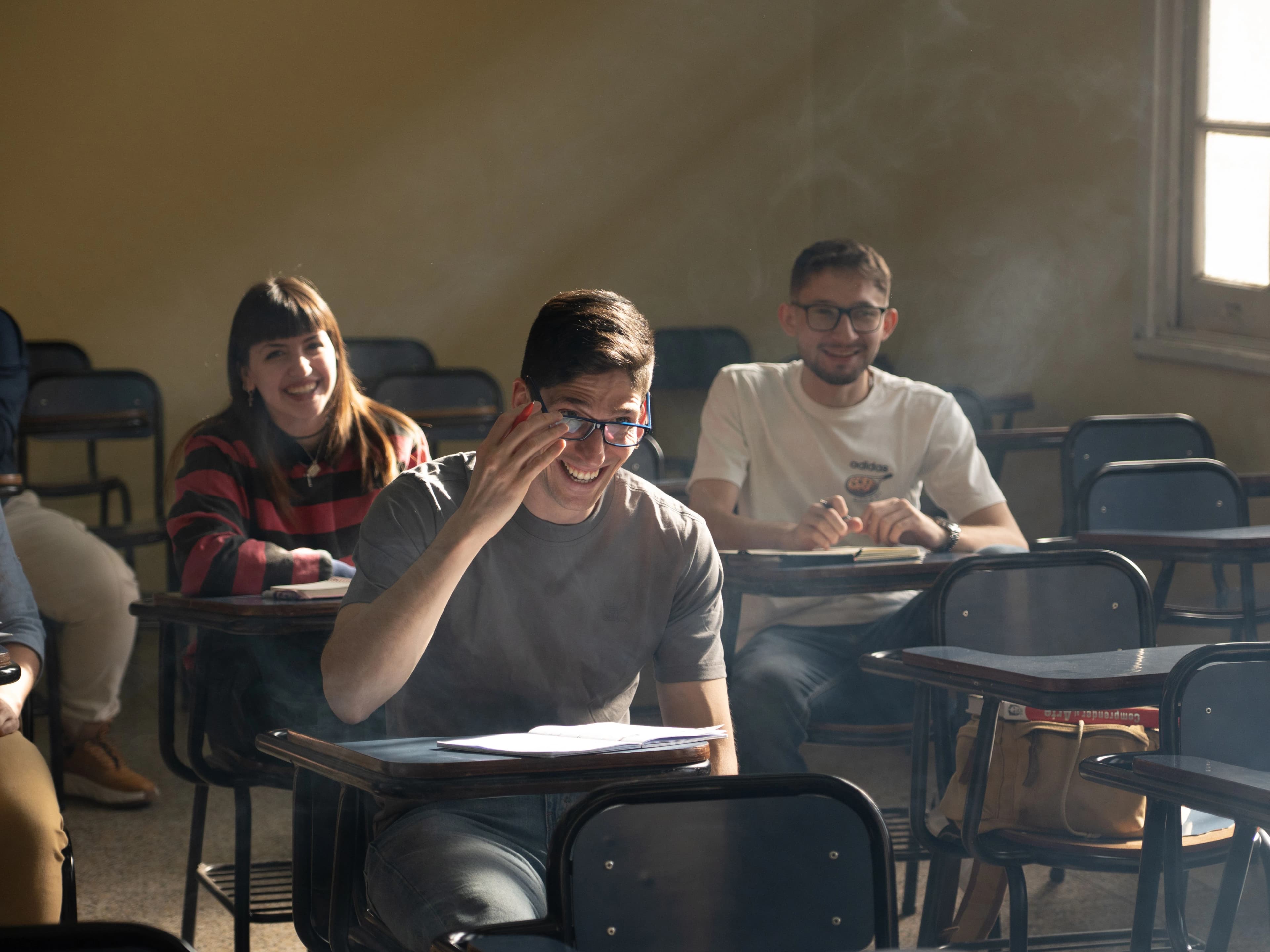 De jeunes étudiants souriants suivent un cours, cahiers ouverts sur leurs pupitres.