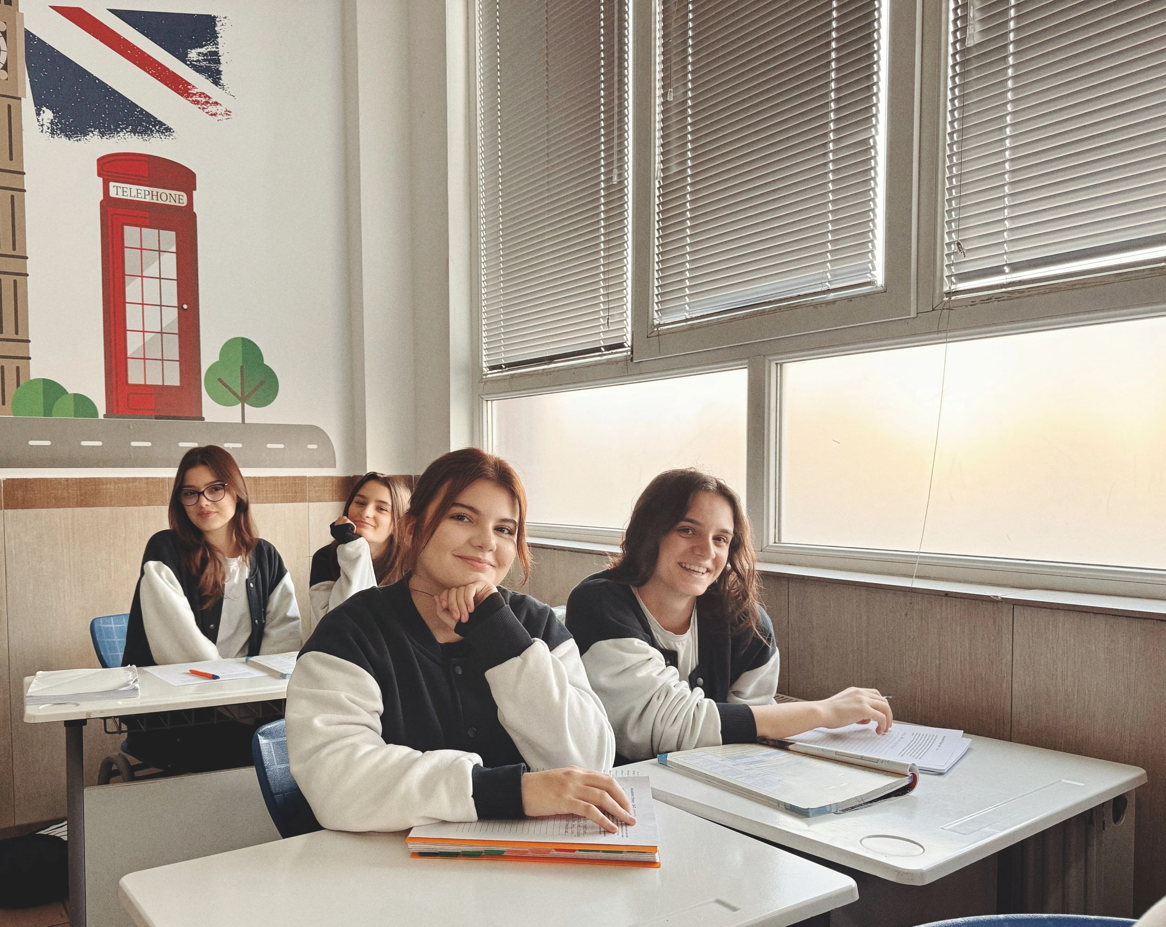 Quatre lycéens souriants assis à leurs tables pendant un cours, cahiers ouverts.