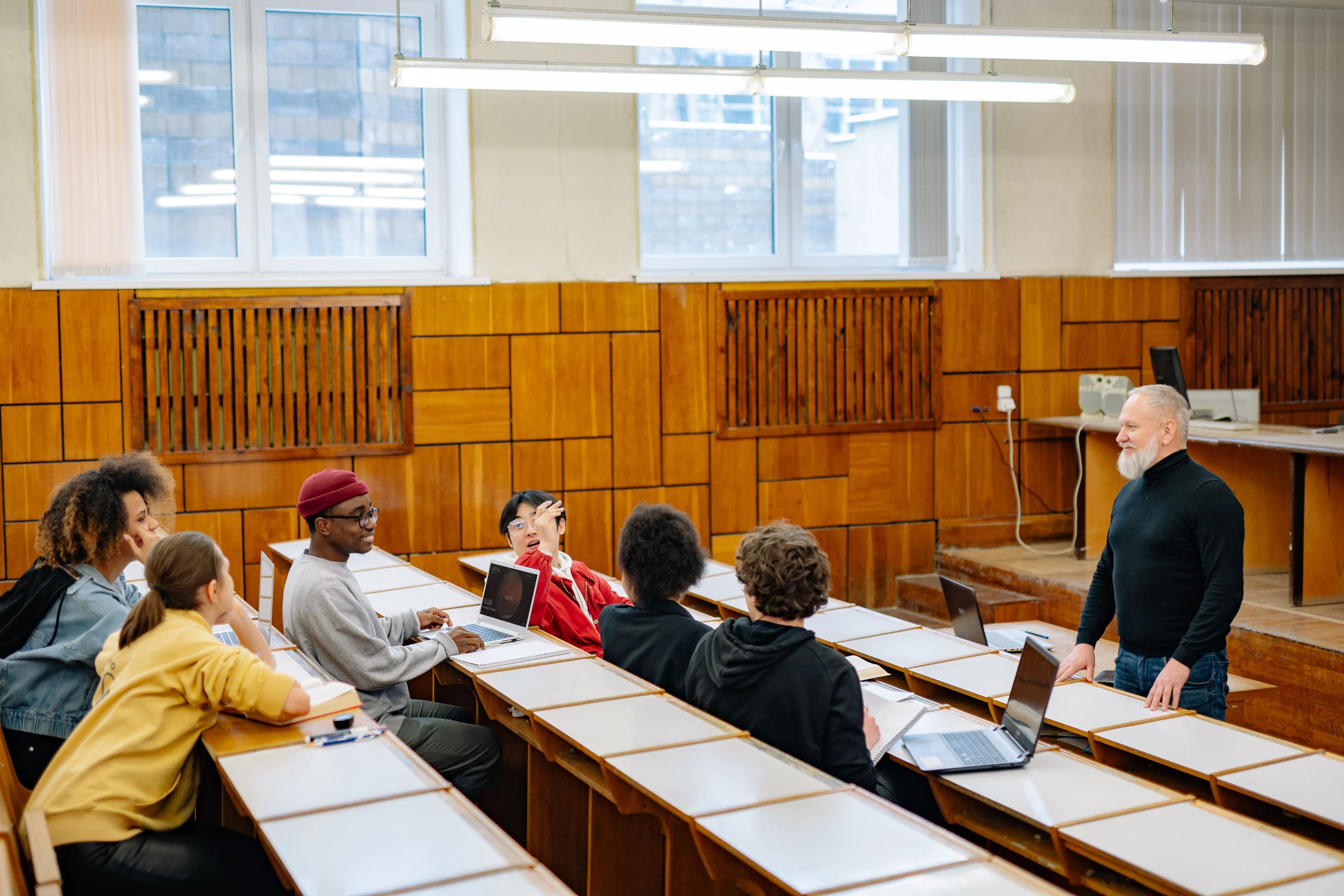 Un enseignant échange avec un groupe d’étudiants installés dans un amphithéâtre, ordinateurs ouverts.