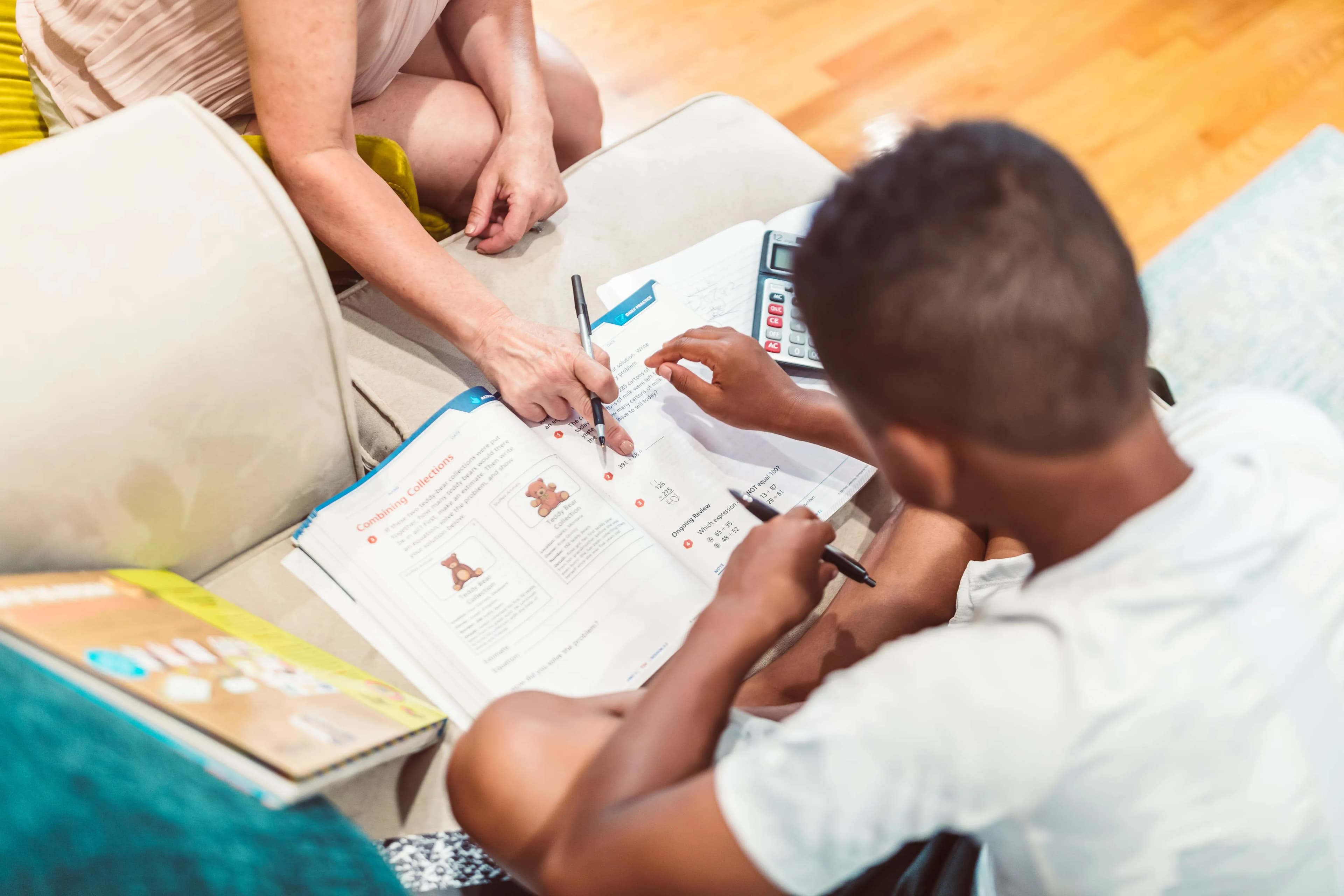 Vue de dessus : une personne aide un adolescent à résoudre un exercice de maths dans un cahier.