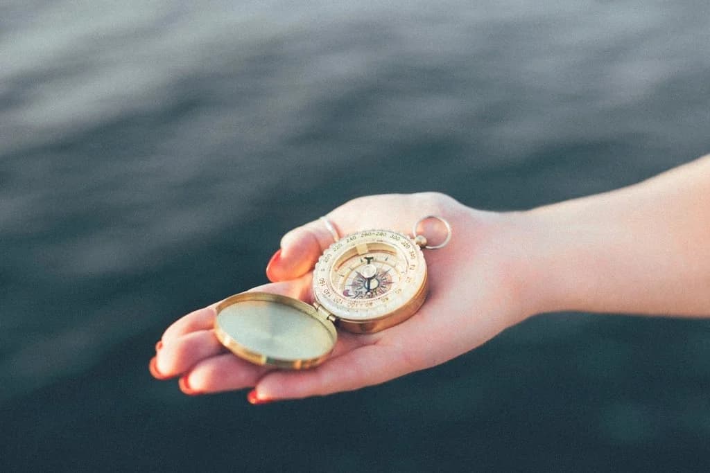 Une main tient une boussole dorée au-dessus de l’eau, symbole de l’orientation à trouver.