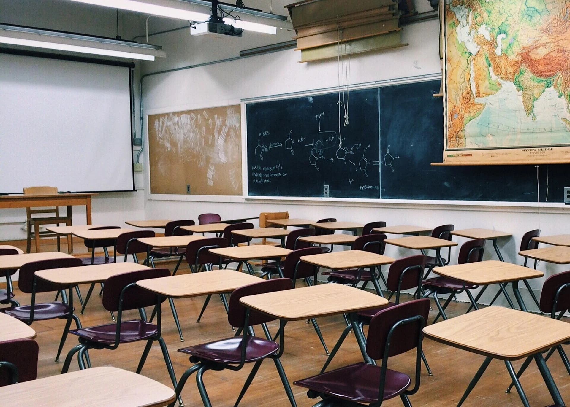 Une salle de classe vide, tables et chaises alignées face au tableau noir.