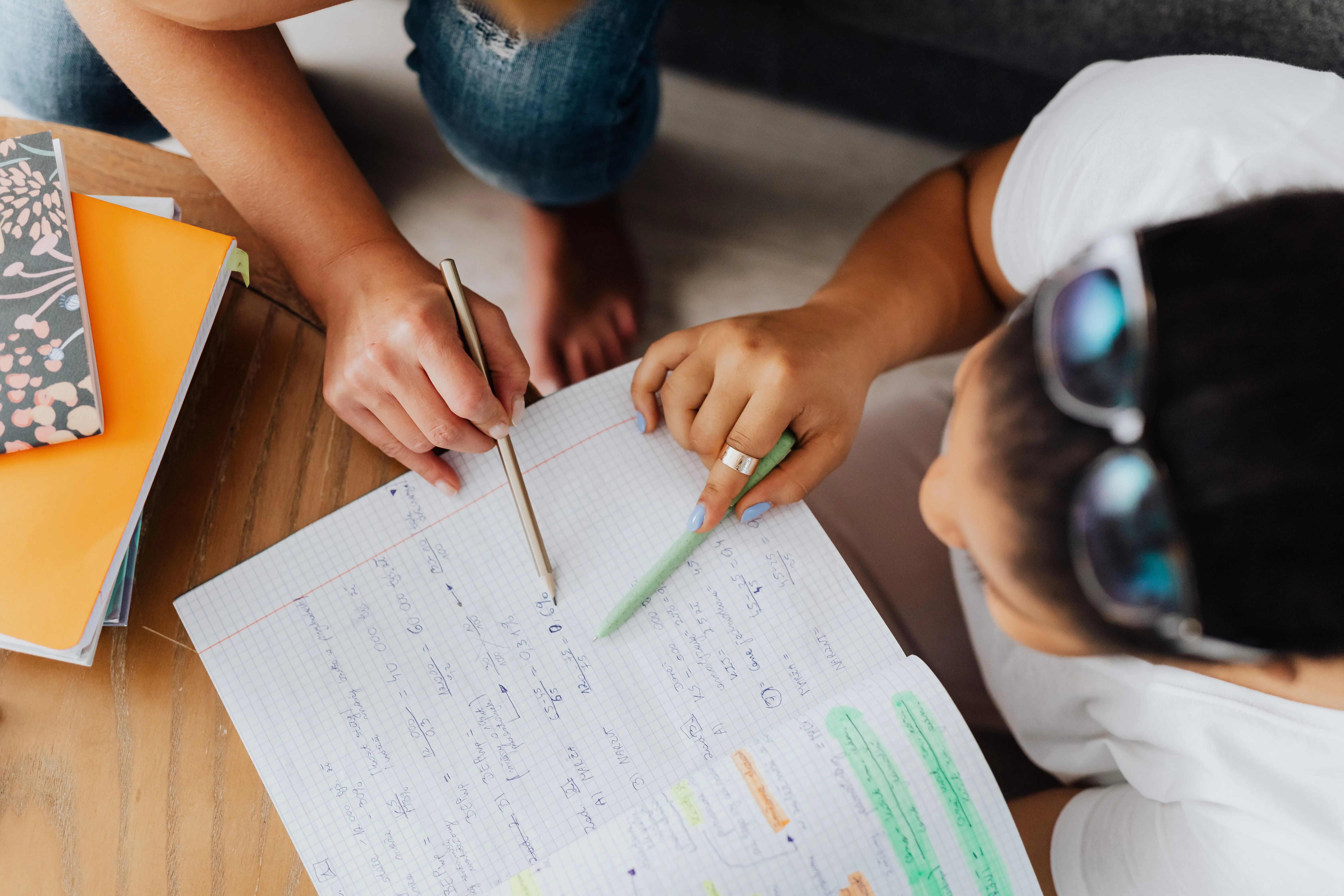 Vue de dessus : deux personnes travaillent ensemble sur des notes de maths manuscrites sur une feuille quadrillée.